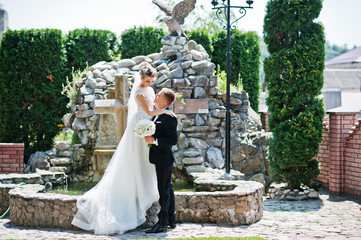 Stylish wedding couple near cross with fountain.