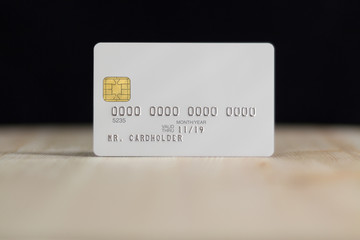 White credit card with embossing on wooden table over black wall, shallow depth of field