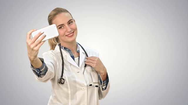 Young pretty female doctor makes selfie on smart phone on white background.