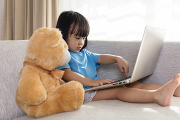 Asian Chinese little girl using laptop with teddy bear