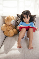 Asian Chinese little girl reading book with teddy bear