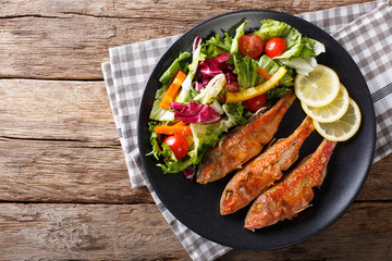 Roasted red mullet with fresh vegetables and lemon close-up. horizontal top view