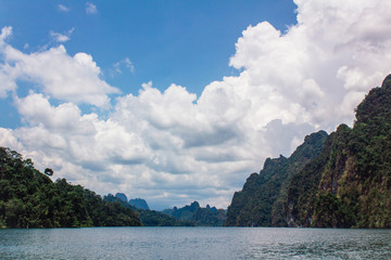 River flowing among green cliffs. Tropic river flowing along green rocky cliffs under blue sky with white soft clouds.