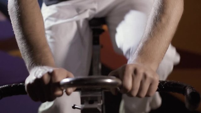 Concentrated young sporty man working out on stationary bike in studio at night