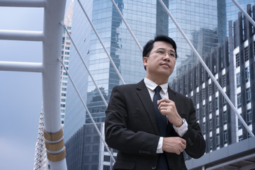 Asian confident Businessman standing in suit and looking away with modern city background