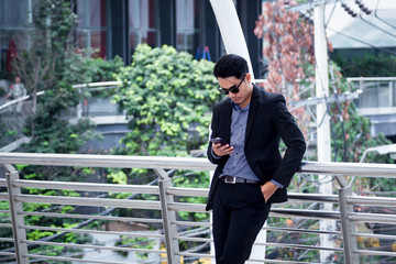 asian business man standing and use smartphone with business building background