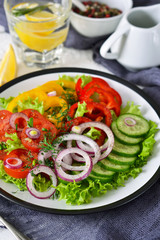 Vegetable mix salad with avocado and olive oil sauce on a white, wooden background.