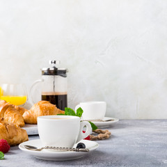 White cups of coffee and croissants on light gray background, selective focus. Healthy breakfast concept with copy space.