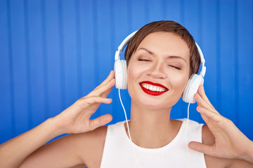 Naklejka premium Enjoying the sound. Colorful portrait of happy young woman with white earphones is listening music.