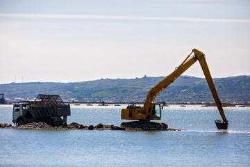 an excavator loads a dump sand in the water