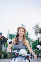 Riding lifestyle. Outdoor portrait of pretty young woman in hat sitting on scooter.