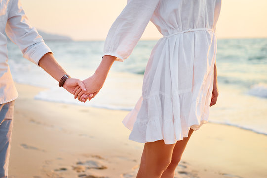 Honeymoon. Close up of loving couple holding hands on a beach near the sea.