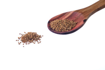 Fenugreek seeds on a brass spoon isolated on a white background.