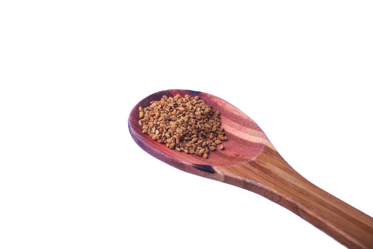 Fenugreek seeds on a brass spoon isolated on a white background.