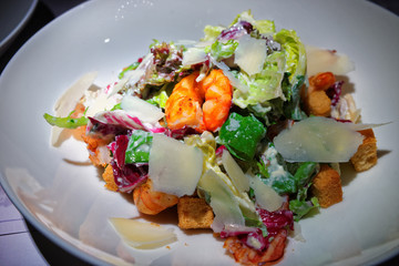 Caesar salad with prawns on white plate
