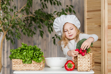 Little beautiful girl making vegetable salad in the kitchen. Healthy food. Little housewife