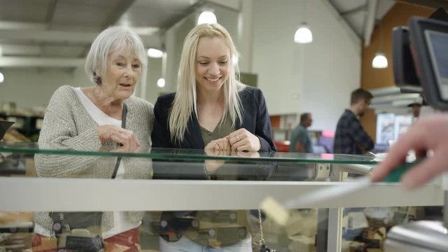  Senior lady & adult granddaughter tasting cheese at deli counter