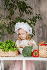 Little beautiful girl making vegetable salad in the kitchen. Healthy food. Little housewife