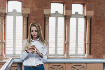 Young female with the phone near the handrail. Horizontal indoors shot.