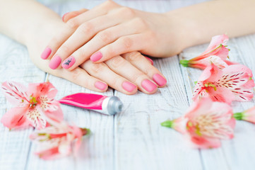 Woman hands with pink manicure on finger nails, delicate flowers and hand lotion tube