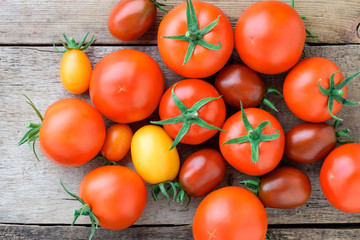 Fresh juicy tomatoes of different varieties on an old wooden table. Tomatoes on a wooden background top view