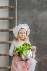 Little beautiful girl holding a pot full of vegetables. Healthy food. Harvest. Little housewife
