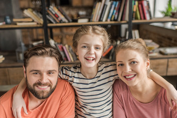 Happy young family with one child embracing and smiling at camera