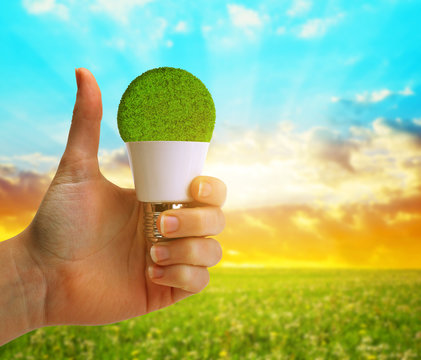 Hand with thumb up holding a eco LED bulb at sunset. Energy saving lamp.