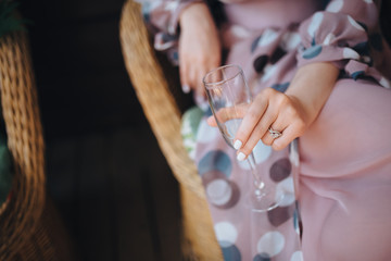 A girl in a bathrobe sits in a chair on the patio and holds a glass in her hand
