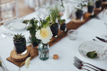 On a serving buffet table there are compositions of flowers and plants in glass and ceramic vases on wooden stands