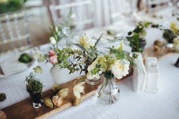 On a serving buffet table there are compositions of flowers and plants in glass and ceramic vases on wooden stands