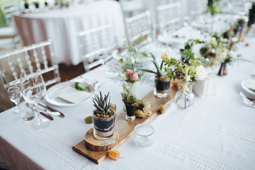 On a serving buffet table there are compositions of flowers and plants in glass and ceramic vases...