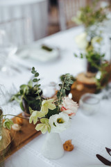 On a serving buffet table there are compositions of flowers and plants in glass and ceramic vases on wooden stands