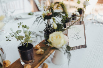 On a serving buffet table there are compositions of flowers and plants in glass and ceramic vases on wooden stands