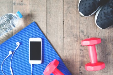 Flat lay of mobile phone with earphones and sport equipments on wood background. Workout and fitness items, top view