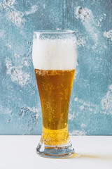 Glass of lager beer with foam on white table with blue texture concrete background. Toned image