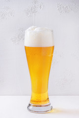 Glass of lager beer with foam on white table with texture concrete background.