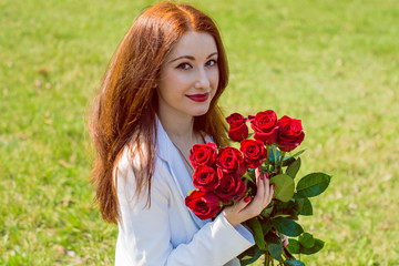 Portrait pretty young redhead european woman in white jacket, asian makeup, with red roses, around garden, grass, have beautiful face, stylish look, necklaces, red nails, hair flapping, windy, sunny