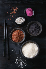 Fototapeta na wymiar Variety assortment of raw uncooked colorful rice white, black, brown, pink in black bowls over burnt wooden background with chopsticks. Top view with space