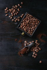 Roasted coffee beans and grind coffee in wood box with scoop over black wooden burnt background. Top view with space.