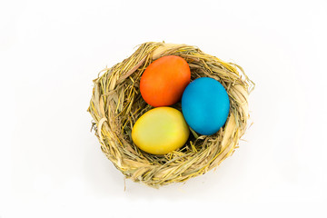 Three chicken eggs painted in bright paint in a nest woven of herbs