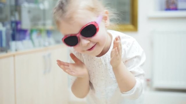 little girl playing and Hamming in front of a mirror and tries fashion medical glasses near mirror - shopping in ophthalmology clinic
