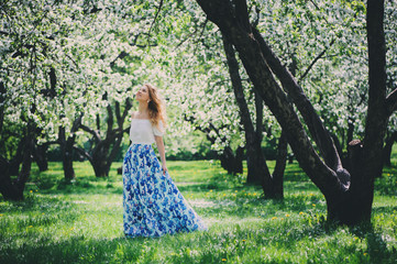 Plakat beautiful young woman in floral maxi skirt walking in spring
