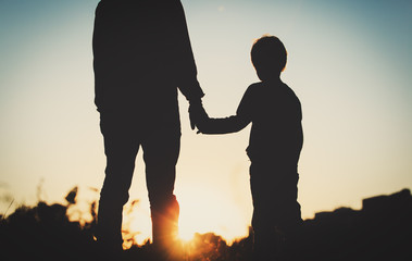 silhouette of father and son holding hands at sunset