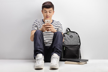 Teenage student leaning against white wall and using phone
