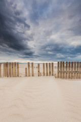 wooden fence on dunes and beach at storm weather