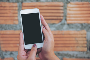 Mockup image of hand holding white mobile phone with blank black screen and brick wall background