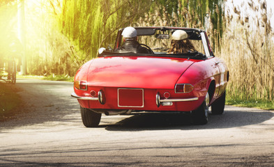 Classic red convertible car traveling in the countryside at sunset - obrazy, fototapety, plakaty