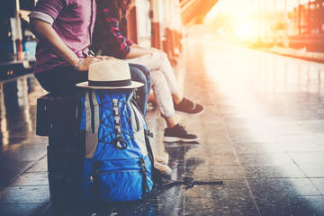 Young tourist couple with backpack sitting on bench at the train station. Two young tourist are waiting to get on the train and begin their journey. Travel concept.