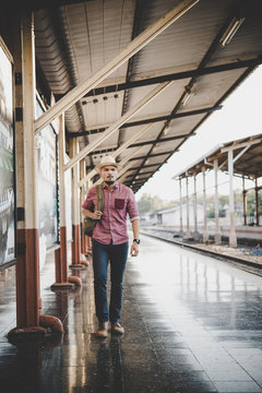 Young tourist man with backpack standing on platform waiting for train at train station, vintage tone filter effects.Travel concept.